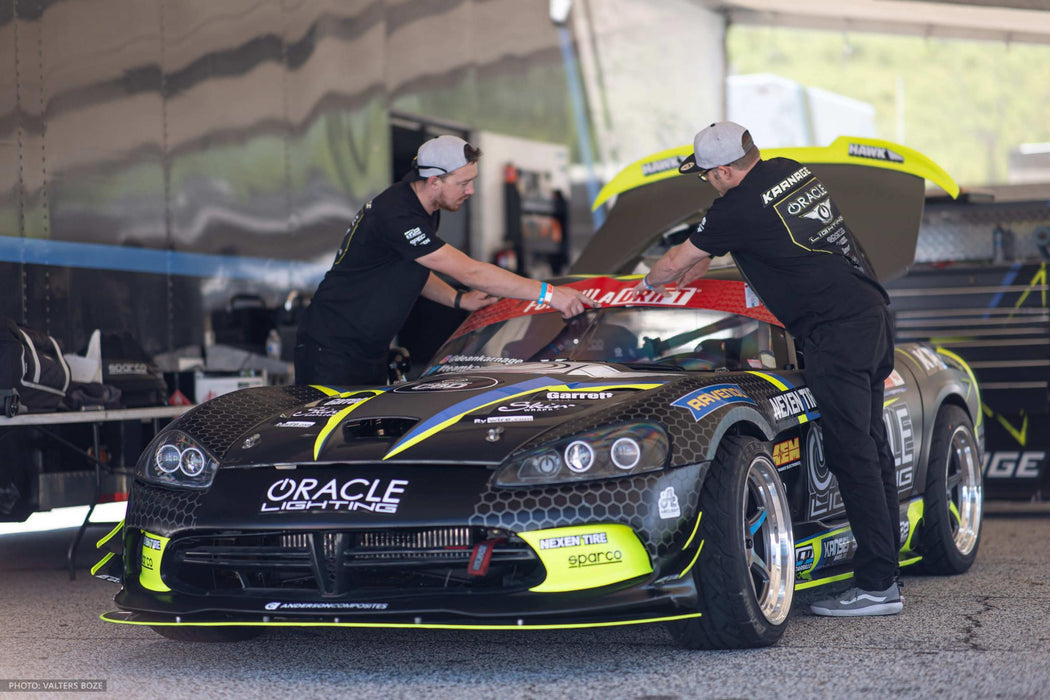 2 People working on a car, both wearing ORACLE Lighting Official Snap-Back Hat.