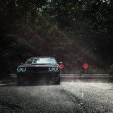 Front view of a black Dodge Challenger, with cyan LED headlight halo rings installed.