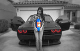 Front view of a girl standing in front of a black Dodge Challenger. The car has red headlight halo rings installed.