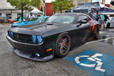 Three quarters view of a black Dodge Challenger parked at a car meet, with white LED headlight and fog light halo rings installed.