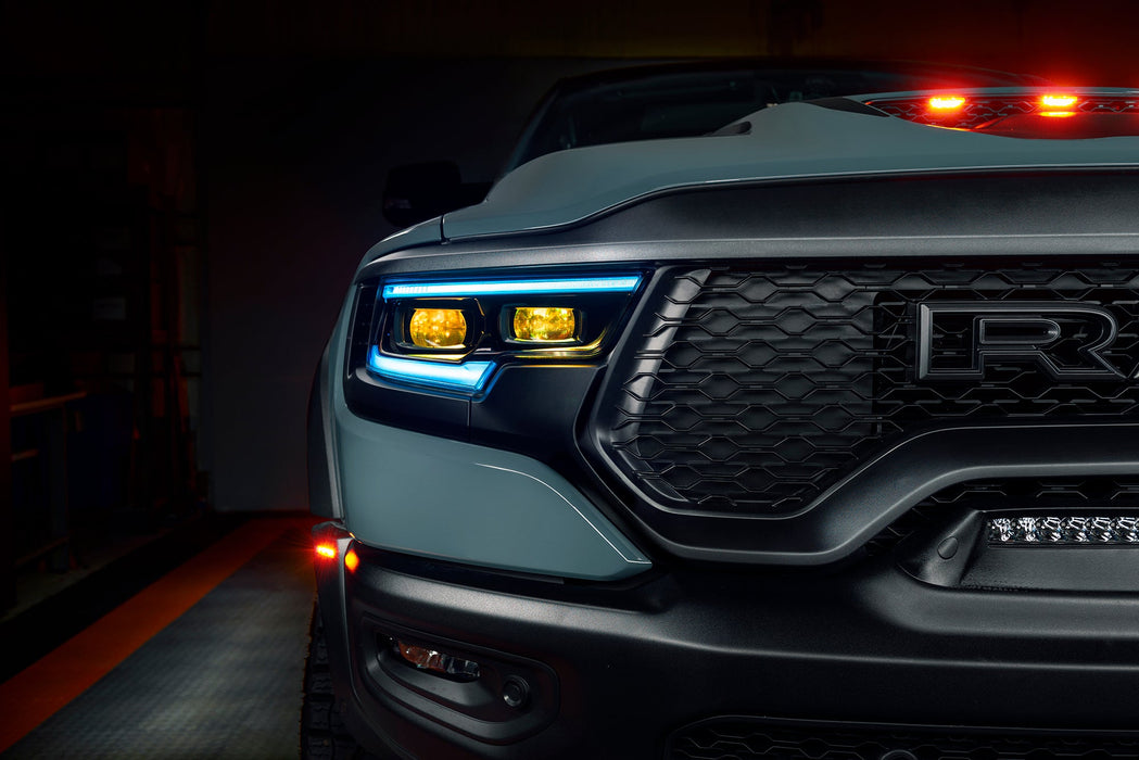 Close-up of Ram 1500 headlights with cyan DRLs and yellow demon eye projectors.