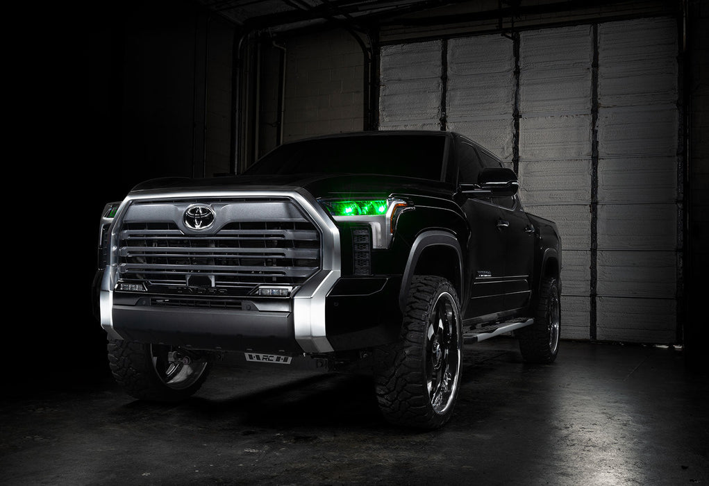 Three quarters view of a black Toyota Tundra with green demon eye projectors.