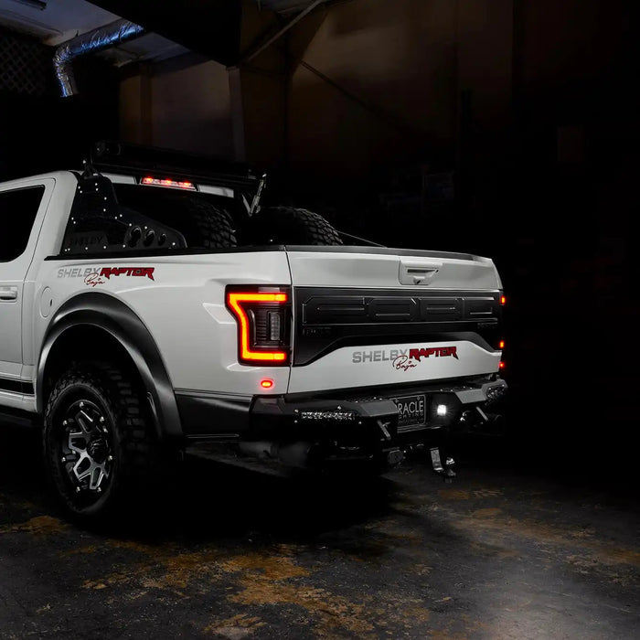 Rear three quarters view of white Ford Raptor with running lights on 