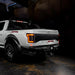 Rear three quarters view of white Ford Raptor with running lights on 