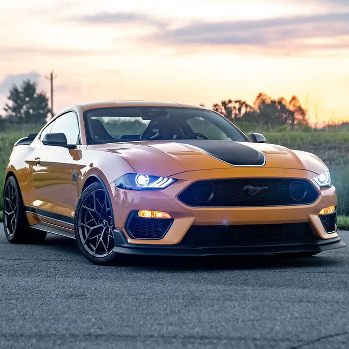 Three quarters view of orange Ford Mustang with bright white LED headlights.
