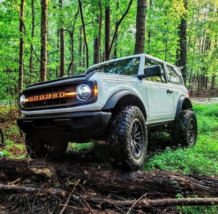 White Ford Bronco in the forest with Amber LED Illuminated Letter Badges installed.