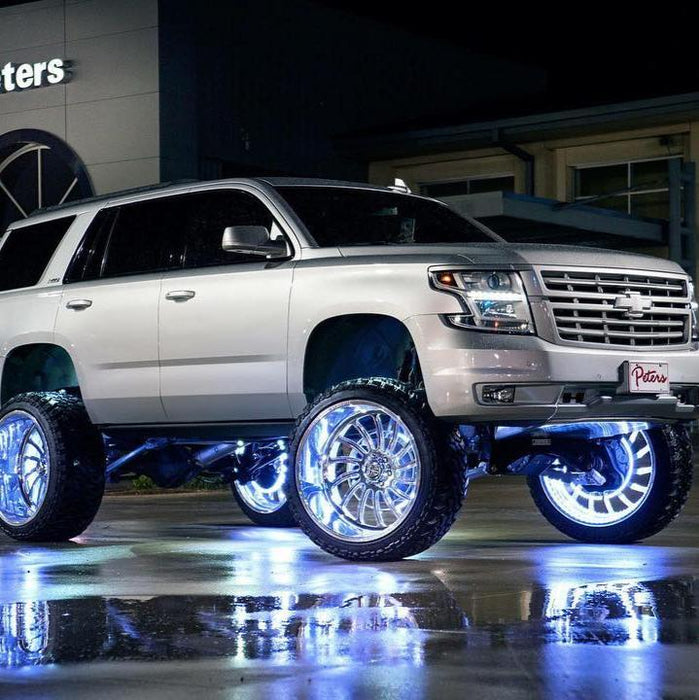 A silver lifted Chevrolet with white LED wheel rings installed, and the bright LEDs reflecting off the wet pavement.