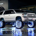 A silver lifted Chevrolet with white LED wheel rings installed, and the bright LEDs reflecting off the wet pavement.