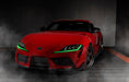 Three quarters view of a red Toyota Supra with green headlight DRLs.