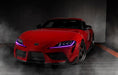 Three quarters view of a red Toyota Supra with pink headlight DRLs.