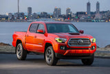 Three quarters view of a red Toyota Tacoma with yellow headlight DRLs.