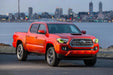 Three quarters view of a red Toyota Tacoma with yellow headlight DRLs.