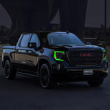 Three quarters view of a black GMC Sierra with green headlight DRLs.