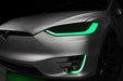 Close-up on the headlights and fog lights of a Tesla Model X with green DRLs.