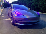 Three quarters view of a Tesla Model 3 with pink headlight DRLs.